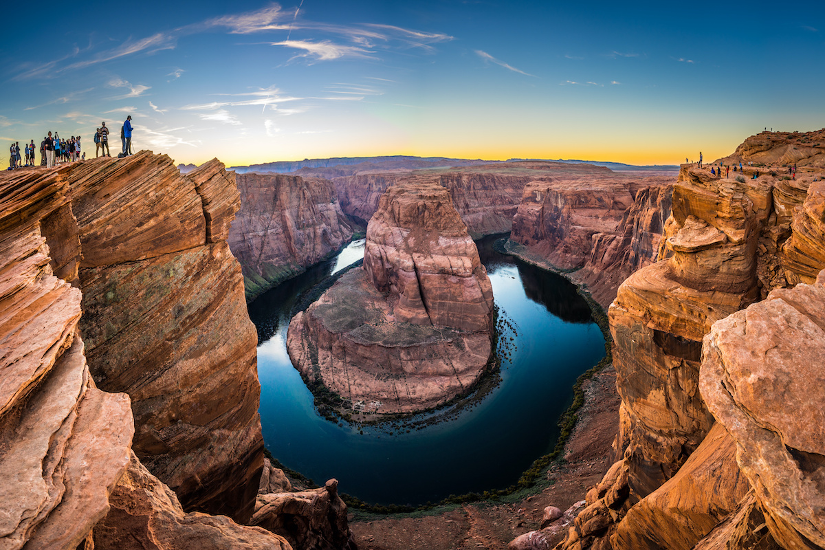 Due miliardi di anni nella roccia! Tutto sul Grand Canyon, dalla storia alle curiosità Sai che affacciarti sul bordo del Grand Canyon significa avere davanti agli occhi quasi due miliardi di anni di storia della Terra? Il Grand Canyon e la sua storia non cominciano con l'uomo, cominciano con l'acqua. Circa sei milioni di anni fa il fiume Colorado ha iniziato a incidere l'altopiano dell'Arizona settentrionale e, scendendo, ha riportato alla luce strati di roccia sempre più antichi, fino a quelli formatisi quasi due miliardi di anni fa. Il risultato è una gola lunga 446 chilometri, profonda fino a 1.857 metri e larga da 500 metri a 29 chilometri. I numeri, però, raccontano solo metà del viaggio. L'altra metà appartiene a chi in questa gola vive da almeno diecimila anni, a chi ci è arrivato per caso cercando tutt'altro e a chi si è battuto perché restasse così com'è. Nei prossimi paragrafi ripercorreremo insieme la storia di questa splendida gola, e ti sveleremo cinque curiosità da conoscere prima di partire. Come si è formato il Grand Canyon? La sua storia Il canyon si apre nell'angolo sud-occidentale del Colorado Plateau, l'altopiano che attraversa Arizona, Utah, Colorado e Nuovo Messico. La sua forma nasce da due movimenti opposti, la terra che si solleva e il fiume che scava. Il sollevamento viene prima. Circa 75 milioni di anni fa la stessa spinta che ha costruito le Montagne Rocciose ha alzato l'altopiano di alcuni chilometri, dando al Colorado la pendenza per incidere la roccia. Il fiume, però, non taglia la pietra da solo. Durante le piene trascina massi e ghiaia sul fondo, ed è quel materiale a lavorare come uno scalpello. Quanti anni ha allora? I geologi ne discutono ancora. Uno studio pubblicato su Nature Geoscience nel 2014 ha mostrato che alcuni tratti erano già incisi oltre 50 milioni di anni fa, mentre i due segmenti decisivi si sono formati meno di sei milioni di anni fa. Comunque sia andata, il risultato si legge come un libro sfogliato al contrario. Più si scende, più si va indietro nel tempo. Procedendo in questo senso, gli strati che si incontrano sono: gli strati sedimentari superiori. Calcari, arenarie e argilliti depositati nel corso del Paleozoico da mari poco profondi, dune desertiche e paludi costiere; la Great Unconformity. Un contatto netto tra rocce di età molto diverse, dove manca all'appello un lunghissimo capitolo geologico. È uno degli enigmi più studiati al mondo; le rocce del basamento. Sul fondo, vicino al fiume, gli scisti e i graniti più antichi del canyon, formatisi quasi due miliardi di anni fa. I colori che si vedono dal bordo, dal rosso all’ocra e al grigio dipendono dalla composizione di questi strati e dal ferro che li attraversa. Cambiano con la luce, e per questo il canyon delle otto del mattino non è il canyon delle sei di sera. Lo stesso sollevamento dell'altopiano che ha permesso al Colorado di lavorare così in profondità ha modellato, poco più a nord, gli archi naturali dello Utah e le guglie che si incontrano lungo i sentieri del Bryce Canyon. La roccia, però, è solo il primo capitolo. Chi ha scoperto il Grand Canyon? Dai nativi americani a John Wesley Powell Quando si parla del Grand Canyon e della sua storia, la domanda su chi lo abbia scoperto ha una risposta scomoda: nessuno lo ha scoperto, perché qualcuno c'era già. Le persone abitano questa gola da più di diecimila anni. Oggi, infatti, il National Park Service riconosce 11 tribù tradizionalmente associate al Grand Canyon, tra cui Havasupai, Hualapai, Hopi, Navajo, Zuni, la Yavapai-Apache Nation e diverse bande Paiute. Qui hanno coltivato, cacciato, costruito villaggi e tramandato racconti, e qui continuano a vivere. Il primo europeo ad affacciarsi sul canyon fu lo spagnolo García López de Cárdenas, nel 1540. Faceva parte della spedizione di Coronado e cercava il grande fiume di cui parlavano gli Hopi. Trovò un ostacolo, non una meraviglia, e dopo di lui la gola rimase quasi ignorata per tre secoli. Il vero cambio di sguardo arriva nel 1869 con John Wesley Powell, maggiore e geologo, veterano della Guerra Civile. Con quattro barche e nove uomini scese il fiume Colorado attraverso il canyon: fu la prima spedizione documentata a percorrerlo per intero. Powell descrisse le rocce esposte come le "pagine di un grande libro di storia", e fu lui a diffondere il nome con cui oggi lo conosciamo. La sua impresa aprì la strada a geologi, fotografi e infine viaggiatori. Fu il momento in cui il canyon smise di essere un problema da aggirare e cominciò a essere un luogo da attraversare, lo stesso passaggio che, in altri territori del West, ha segnato i luoghi della storia dei nativi americani. Dal 1893 al parco nazionale, storia del Grand Canyon e della sua tutela Diventare parco nazionale non fu né rapido né scontato. Per decenni la gola interessò soprattutto i cercatori di rame e uranio, e le compagnie minerarie fecero muro contro ogni ipotesi di protezione integrale. Theodore Roosevelt la visitò nel 1903 e ne uscì convinto: quel paesaggio andava lasciato com'era. Usò l'Antiquities Act per dichiararlo monumento nazionale nel 1908, ma servirono ancora undici anni prima che il Congresso lo trasformasse in parco. Il 26 febbraio 1919 il presidente Woodrow Wilson firmò il Grand Canyon National Park Act, trasformando il canyon nel diciassettesimo parco nazionale degli Stati Uniti. Da allora il perimetro si è ampliato e il riconoscimento è cresciuto. Oggi il parco supera i 4.900 chilometri quadrati e nel 2024 ha accolto 4.919.163 visitatori: resta il cuore di ogni itinerario tra i grandi parchi americani. 5 curiosità sul Grand Canyon da conoscere prima di partire Conoscere la storia del Grand Canyon è importante, ma alcune cose si capiscono solo quando qualcuno te le racconta sul posto. Sono i dettagli che raramente si trovano nelle guide e che, una volta noti, cambiano quello che vedi dal bordo: un nome, una data, un vuoto tra due strati di roccia. Ecco, allora, 5 curiosità che vale la pena di conoscere prima di partire. Non è il canyon più profondo del mondo. Altre gole scendono più in basso: il primato del Grand Canyon sta nell'insieme di lunghezza, larghezza e profondità, non in un singolo record. I due bordi sono due mondi diversi. Il South Rim, intorno ai 2.100 metri, è il più accessibile e aperto tutto l'anno. Il North Rim supera i 2.400 metri, è più fresco, molto meno frequentato e chiude nei mesi invernali per la neve. Il capitolo che manca. Lungo la Great Unconformity due strati che si toccano sono separati da un abisso di tempo: geologi da tutto il mondo continuano a studiare dove sia finita la roccia mancante. A dare i nomi fu un uomo con un braccio solo. Powell aveva perso il braccio destro nella battaglia di Shiloh. Molti punti panoramici del bordo sud portano invece i nomi delle tribù native: Hopi Point, Navajo Point, Yavapai Point, Mohave Point. Un nome restituito. Nel 2023 l'oasi lungo il Bright Angel Trail, per decenni chiamata Indian Garden, è tornata a chiamarsi Havasupai Gardens, su richiesta della tribù che vi coltivava fino agli anni Venti. Dal bordo sud tutto questo si legge in un colpo d'occhio, e ogni affaccio ha la propria luce e la propria ora: i punti panoramici del Grand Canyon meritano tempo, non fretta. In viaggio nel Grand Canyon con Utat: due itinerari per viverlo Leggere curiosità sul Grand Canyon, la storia e la sua formazione geologica è una cosa. Sentirla sotto i piedi, con qualcuno accanto che sa spiegarti cosa stai guardando, è un'altra. Noi di UTAT accompagniamo i viaggiatori negli Stati Uniti da oltre novant'anni e conosciamo direttamente i luoghi che proponiamo. Nel nostro catalogo il canyon è tappa di due itinerari pensati per esigenze diverse: Golden West USA — quattordici giorni da Los Angeles a San Francisco. Oltre al Grand Canyon si attraversano Antelope Canyon, la Monument Valley con jeep tour condotto dai Navajo, Arches, Canyonlands, Bryce, la Death Valley e Yosemite; Parks Explorer — nove giorni e dieci parchi nazionali, da Los Angeles a Las Vegas. Una formula più compatta, per chi vuole concentrare in un solo viaggio Grand Canyon, Mesa Verde, Canyonlands e Zion. Se hai dubbi su quale dei due somigli di più al viaggio che hai in mente, contattaci: ne parliamo insieme e scegliamo il periodo giusto per partire. Glossario per il tuo viaggio Colorado Plateau. Vasto altopiano tra Arizona, Utah, Colorado e Nuovo Messico. Il suo lento sollevamento ha permesso al fiume di scavare tanto in profondità. South Rim. Il bordo meridionale del canyon, intorno ai 2.100 metri di quota: il più accessibile, servito e visitato, aperto tutto l'anno. North Rim. Il bordo settentrionale, oltre i 2.400 metri: più fresco e più appartato, chiuso ai visitatori nei mesi invernali. Great Unconformity. Il contatto tra rocce di età molto distanti visibile lungo le pareti, dove manca un lunghissimo intervallo di tempo geologico. Antiquities Act. Legge statunitense del 1906 che consente al Presidente di istituire monumenti nazionali senza passare dal Congresso.